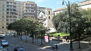 A street with multi-story residential buildings, a church with a bell tower, and trees lining the sidewalk. - Riviera Luxury Suites B&B (Naples)