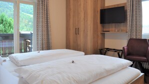 Quarto de hotel com duas camas, televisão e vista para o verde lá fora.