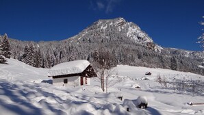 Paisagem coberta de neve, com uma cabana de madeira e uma montanha ao fundo.