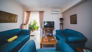 Ein Wohnzimmer mit zwei blau gemusterten Sofas, einem Holztisch, einem Fernseher auf einem Schrank und einem Blumentopf.