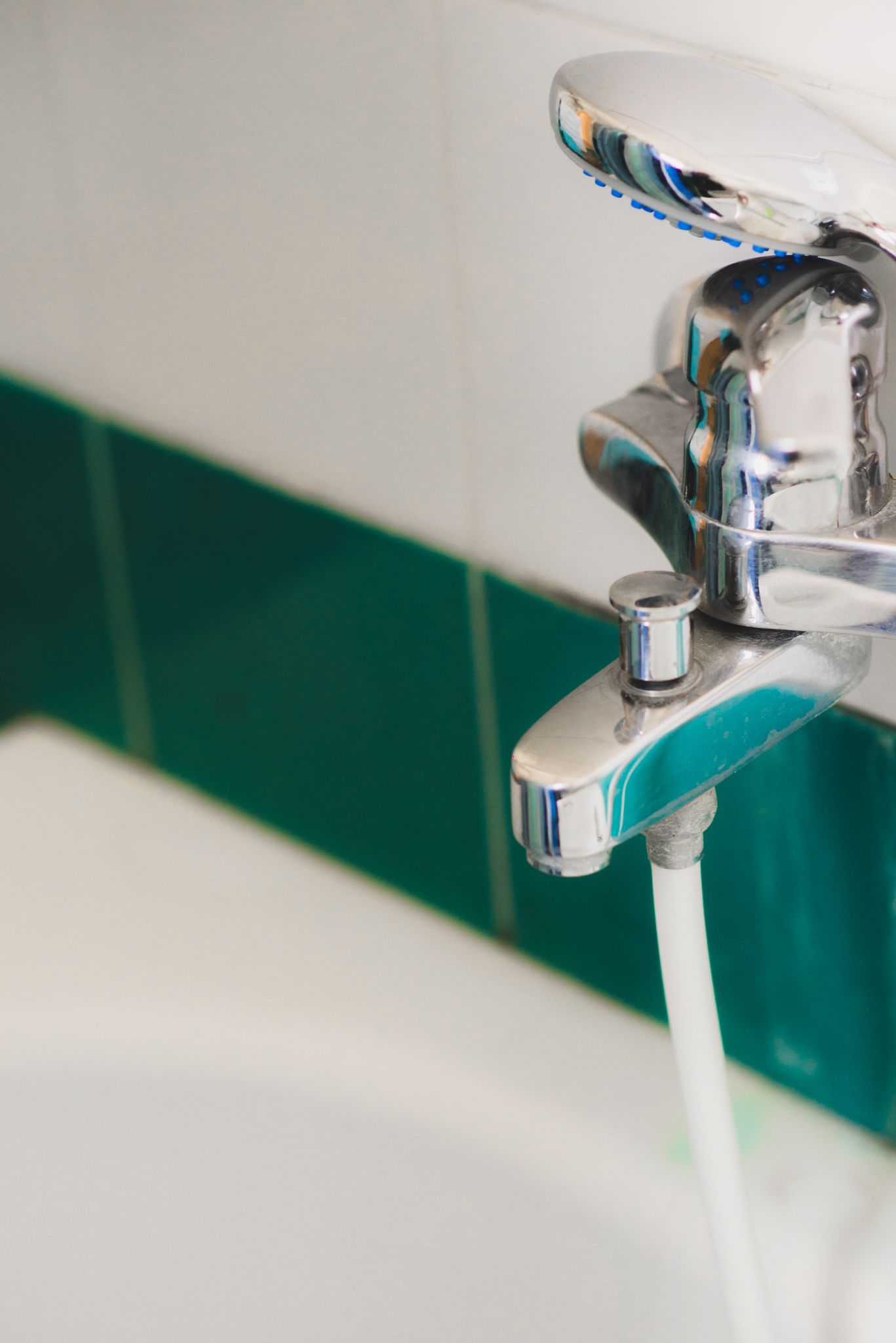 Un baño con grifo cromado y pared de azulejos verdes y blancos.