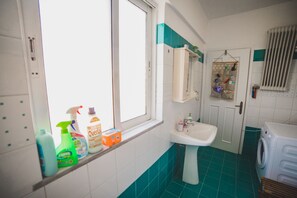 Un baño con ventana, lavamanos, espejo y lavadora.