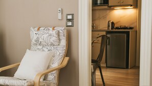 A chair with a leaf pattern, a small table, and a kitchen area with a refrigerator and a kettle. - Casa Mia Apartments (Agios Nikolaos)