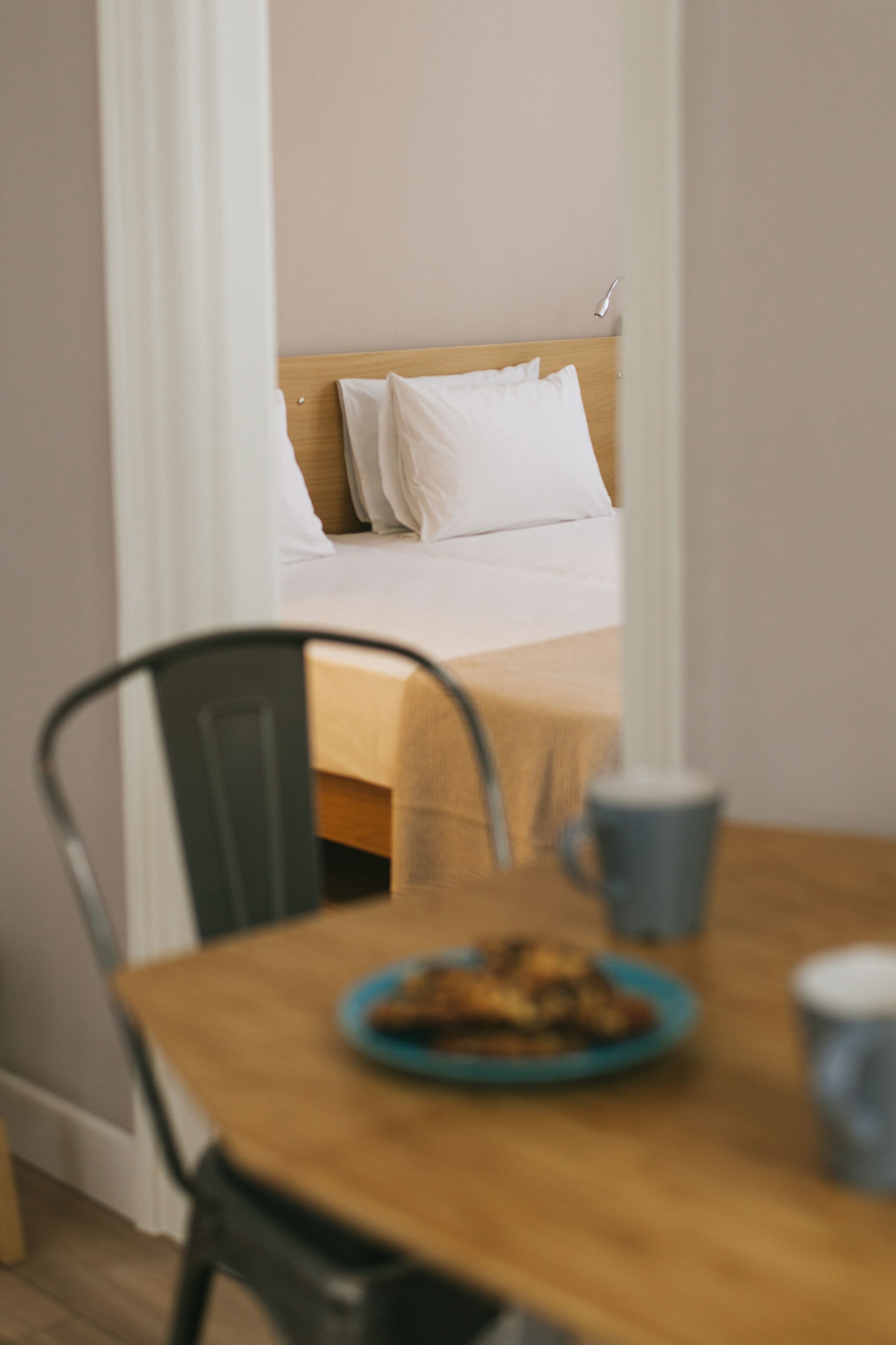 A room with a bed, a table with a plate of food, and a chair.