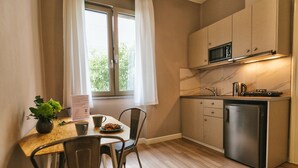 A compact kitchen with a microwave, stove, and refrigerator. There is a dining table with chairs and a small potted plant. - Casa Mia Apartments (Agios Nikolaos)