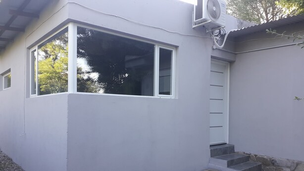A modern building with a large window, a small door, and a set of steps leading to a door. - Casita del Sauce (Sierra de la Ventana)