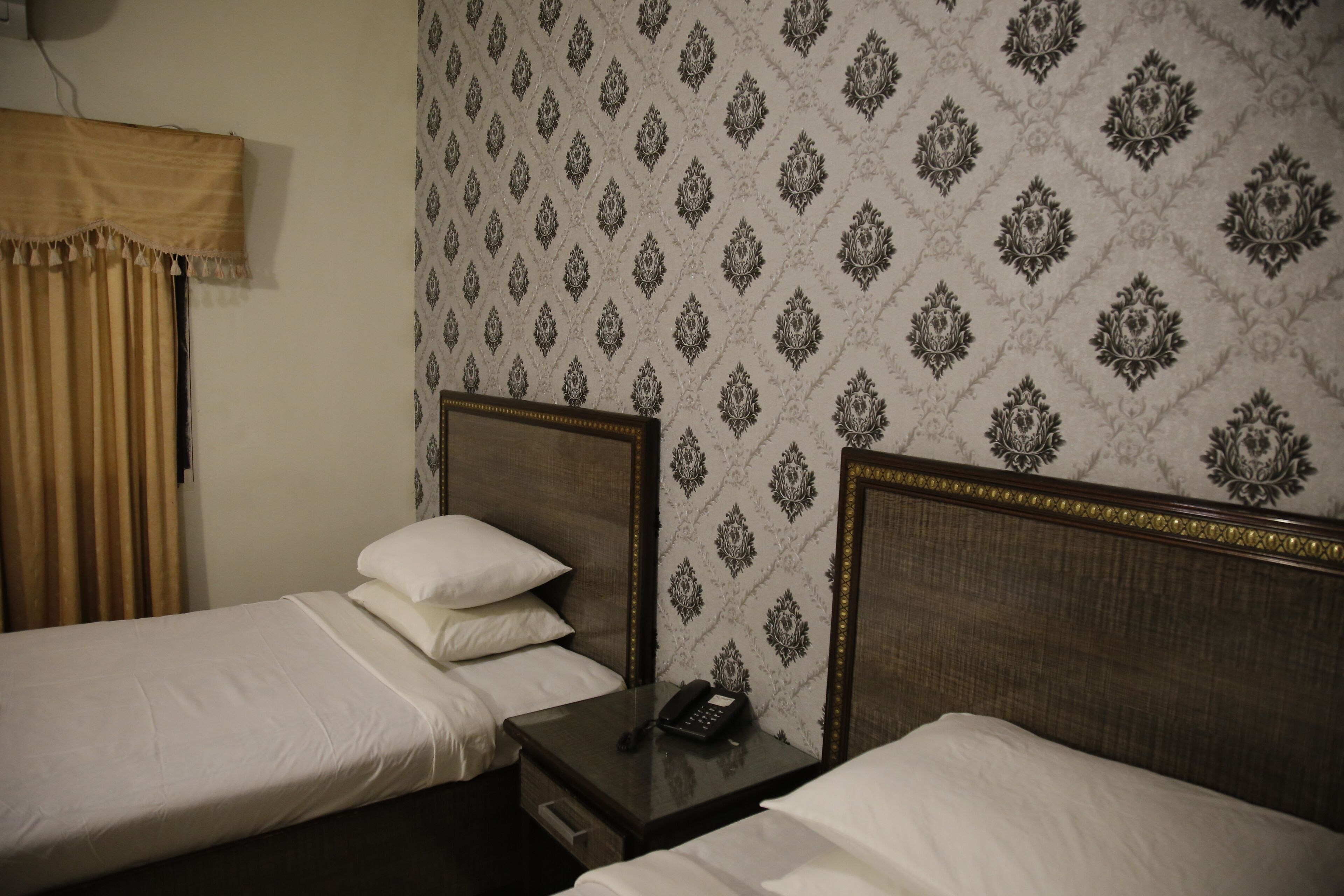 Quarto de hotel com duas camas de solteiro, mesa de cabeceira com telefone e papel de parede estampado.