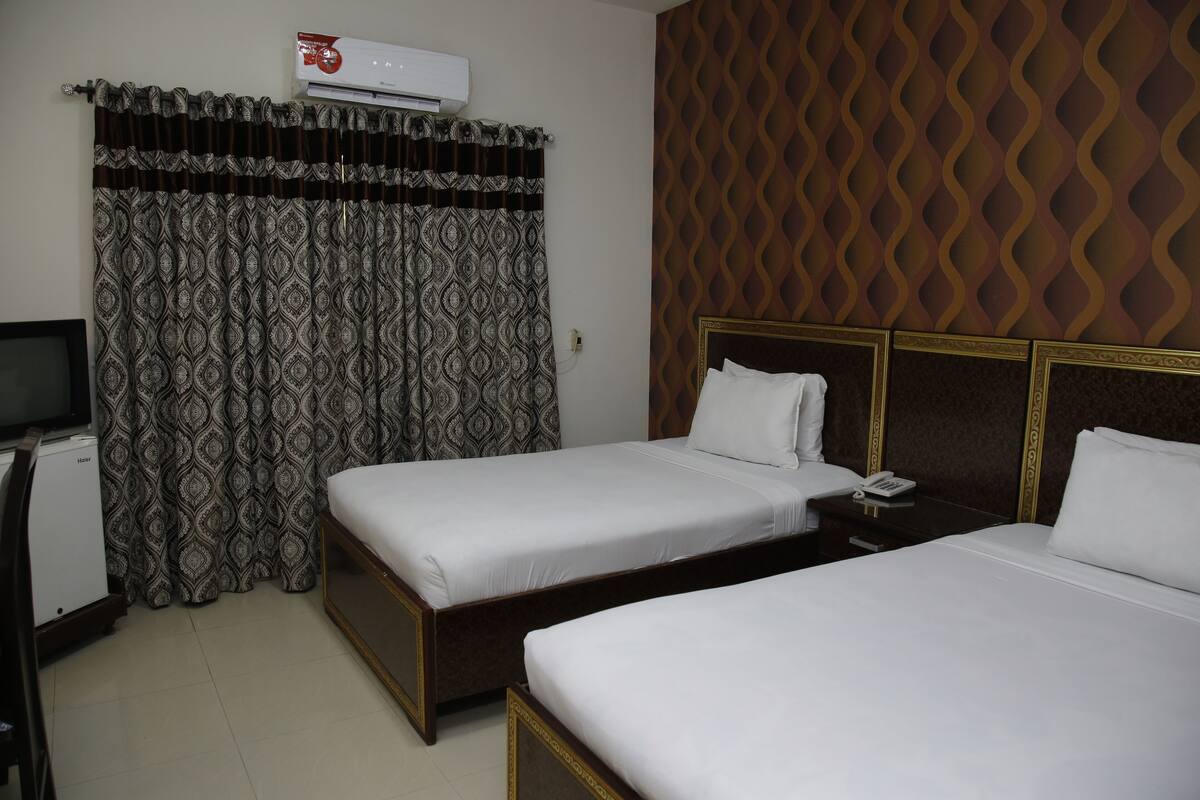 A hotel room with two single beds, a TV, and an air conditioning unit.