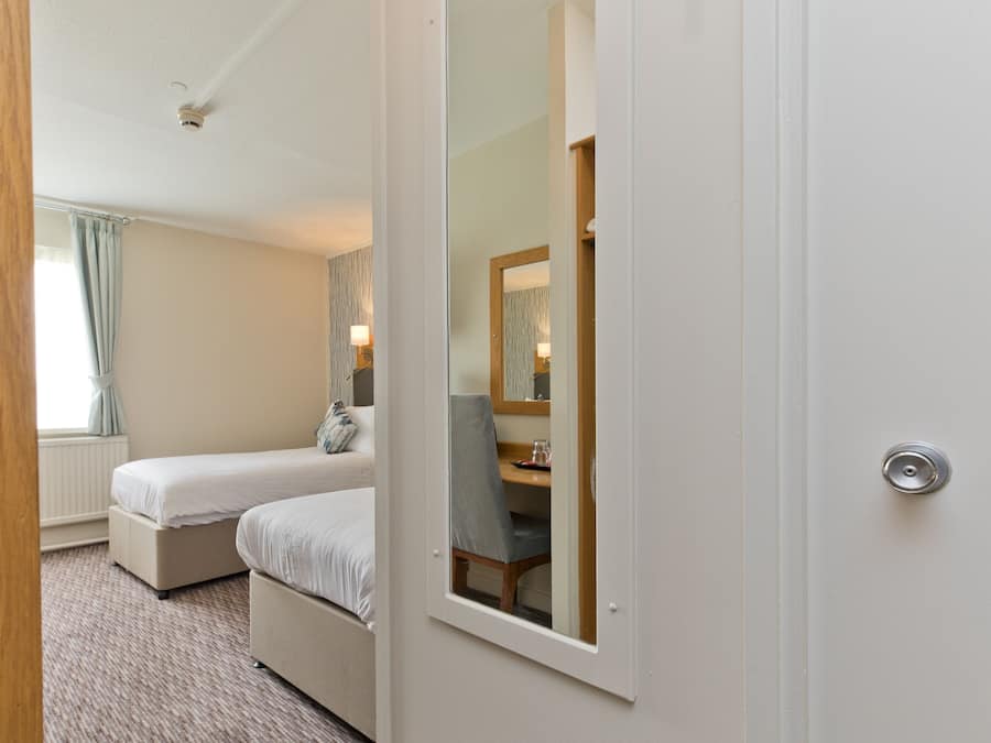 Habitación de hotel con cama, mesita de noche, una silla y un espejo.