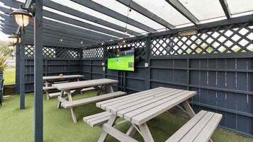Une terrasse extérieure avec des tables de pique-nique et un écran de télévision.