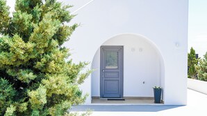 A white building with a dark blue door and a potted plant on the porch. - Saint Apostles (Santorini)