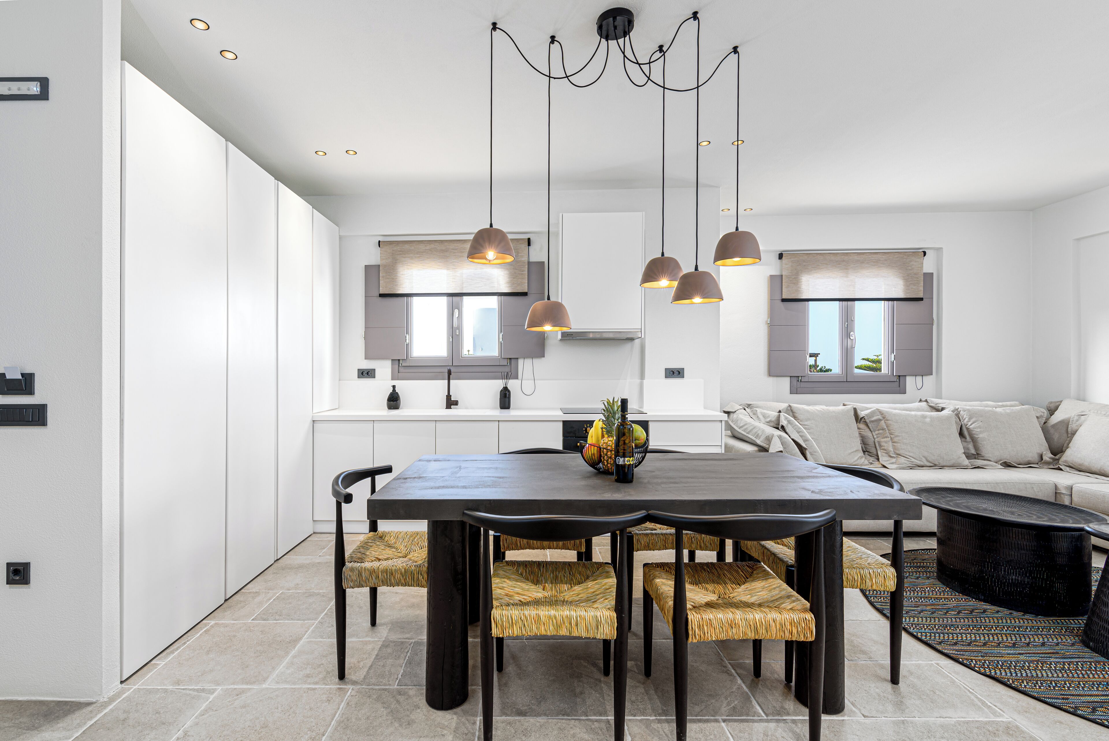 Een moderne keuken met een eethoek, met een donker houten tafel, geweven stoelen en hanglampen.