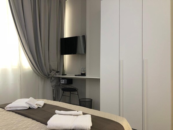 A hotel room with a bed, a desk with a TV, a chair, and a wardrobe.