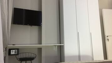 Quarto com cama, televisão na parede, guarda-roupa e secretária com cadeira.