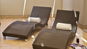 Un balcon doté de deux fauteuils de relaxation en osier, d’un sol carrelé et offrant une vue sur une étendue d’eau et une végétation luxuriante.