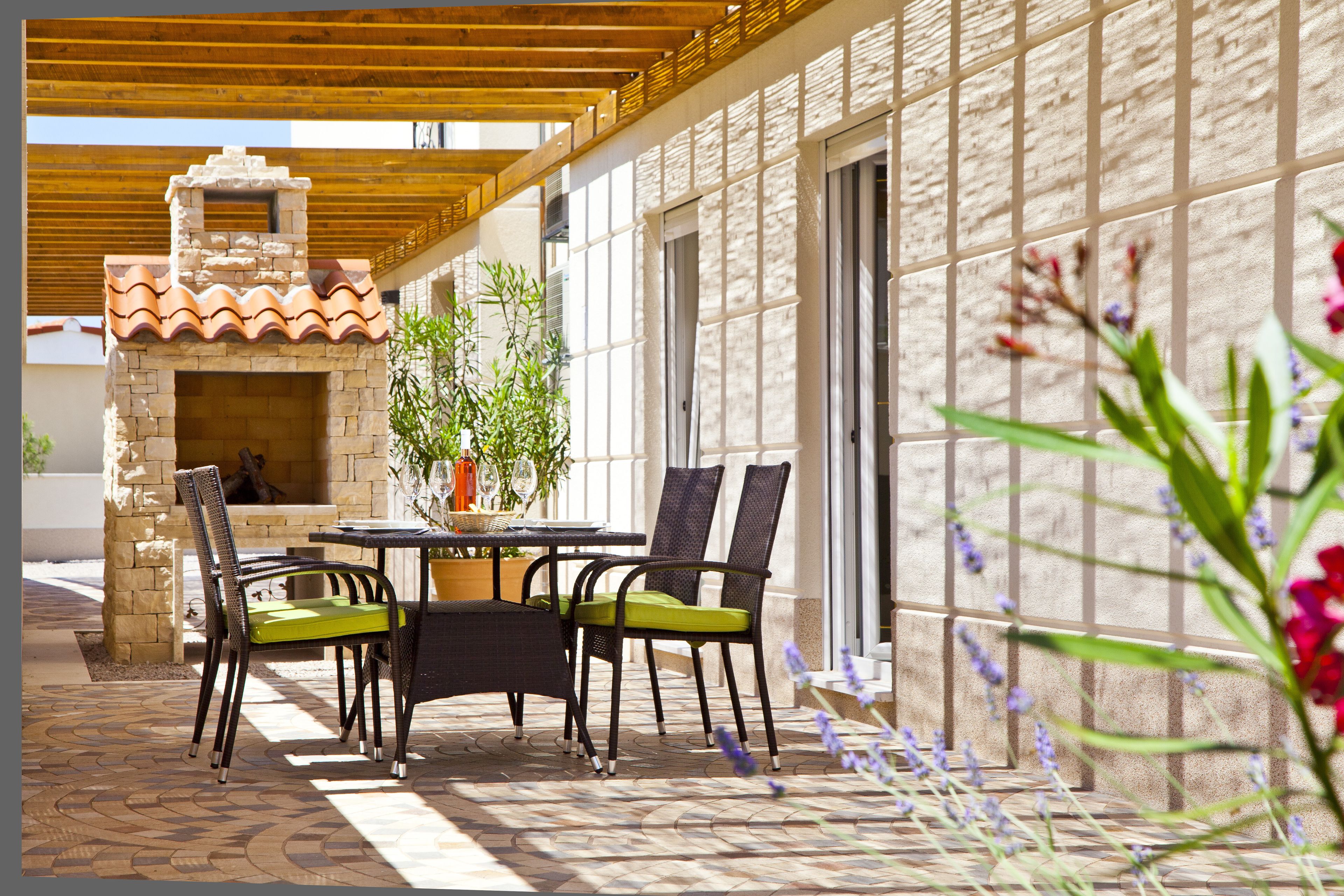 Um pátio externo com lareira de pedra, cadeiras de vime e piso de azulejos.