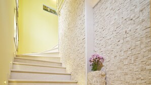 Un escalier aux marches de couleur beige menant à un palier, un mur à texture et un vase rempli de fleurs sur le palier.