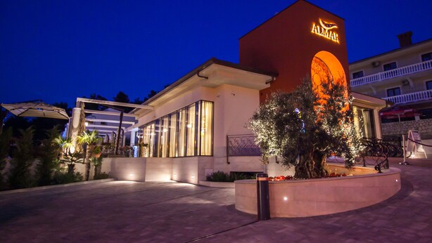 Un hôtel au design moderne, doté d’une enseigne lumineuse bien visible, d’un espace extérieur couvert avec des sièges et d’un jardin aménagé.