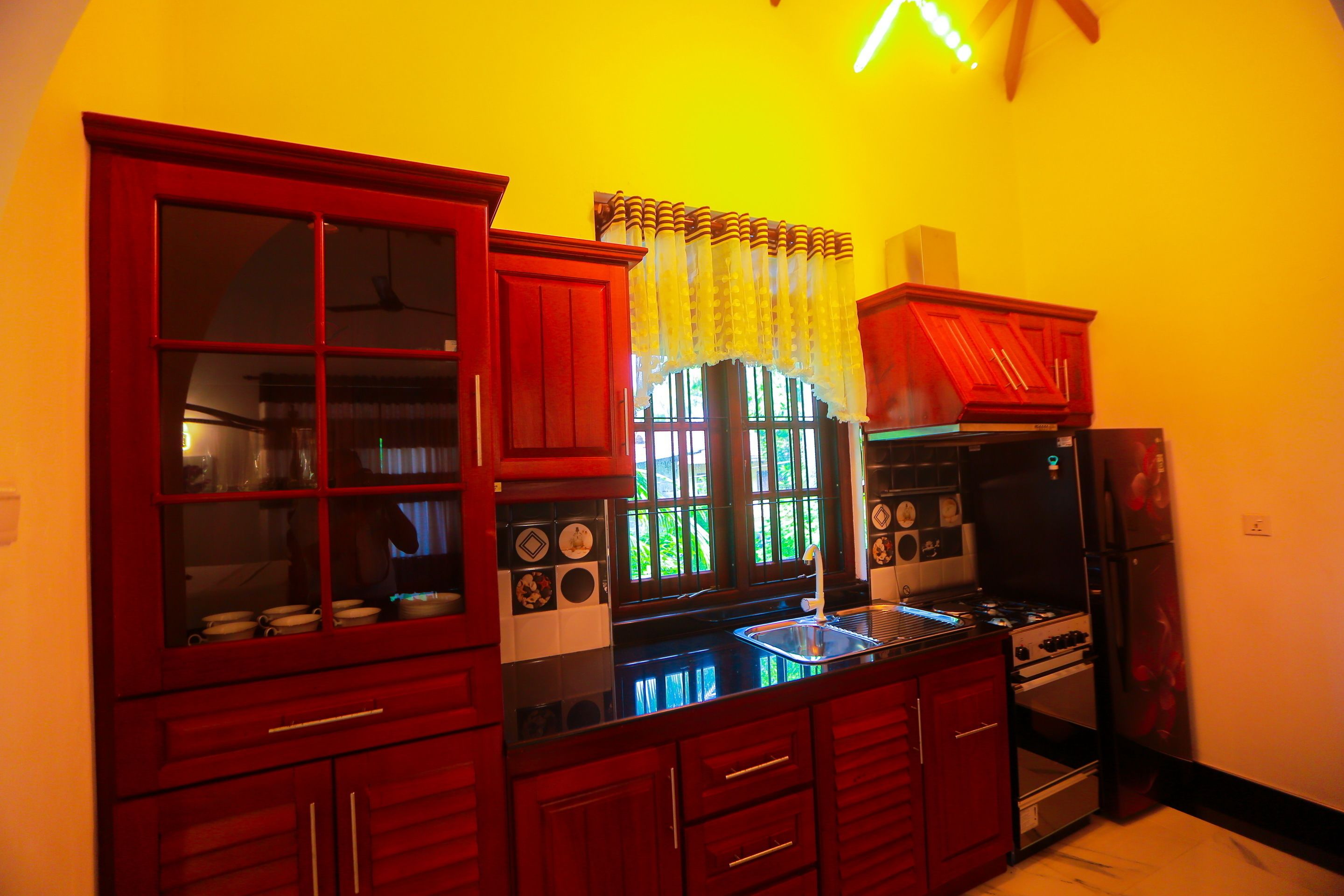 Una cocina con armarios rojos, una encimera negra y una ventana con cortina de encaje.