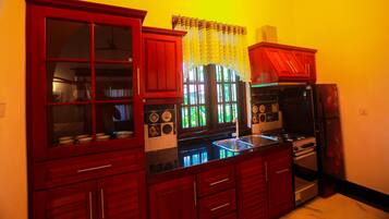 Una cocina con armarios rojos, una encimera negra y una ventana con cortina de encaje.