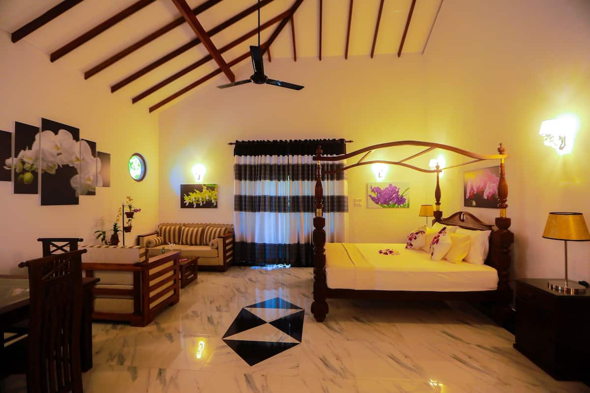 A hotel room with a bed, a sofa, a dining table, and a ceiling fan.