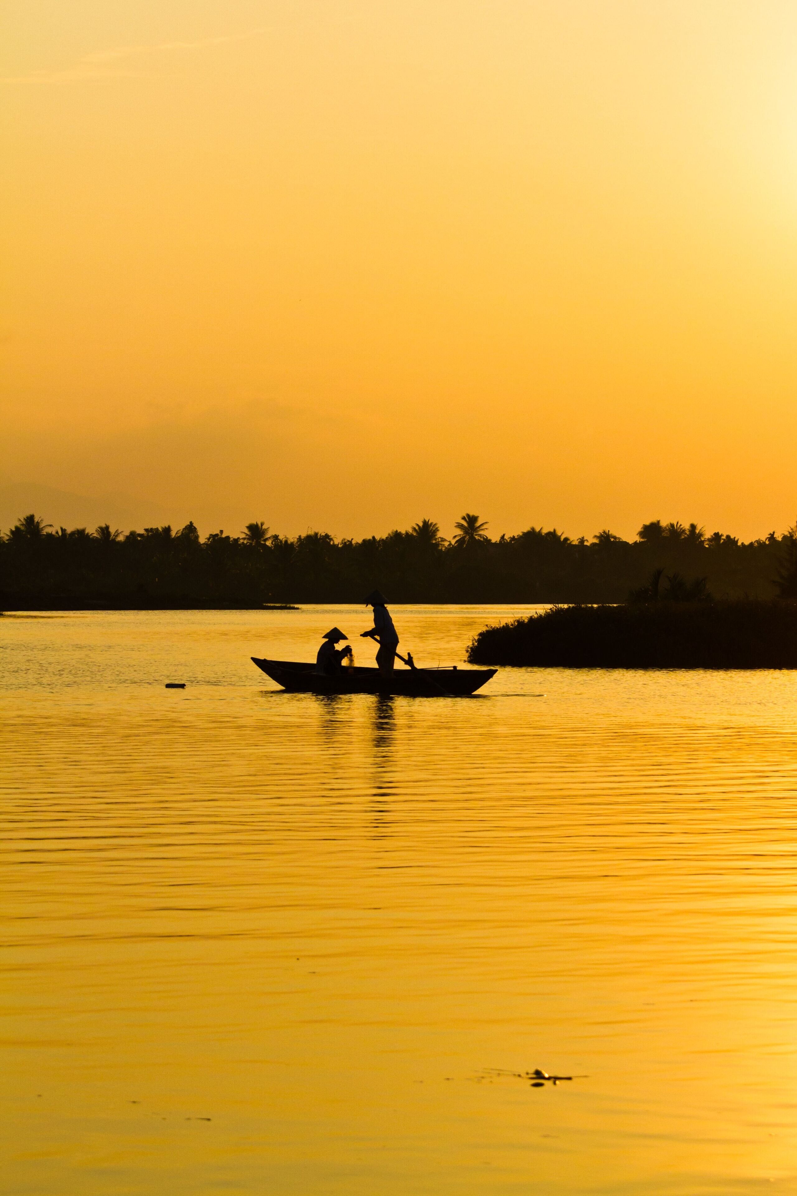 Un coucher de soleil sur une étendue d’eau calme, avec un bateau transportant deux personnes.