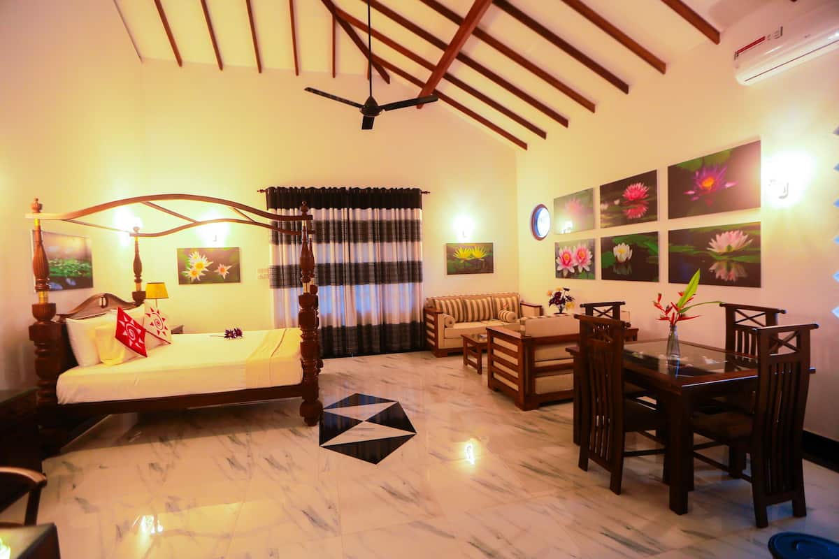 A well-lit living room with a sofa, a dining table with chairs, a bed with a headboard, and a ceiling fan.