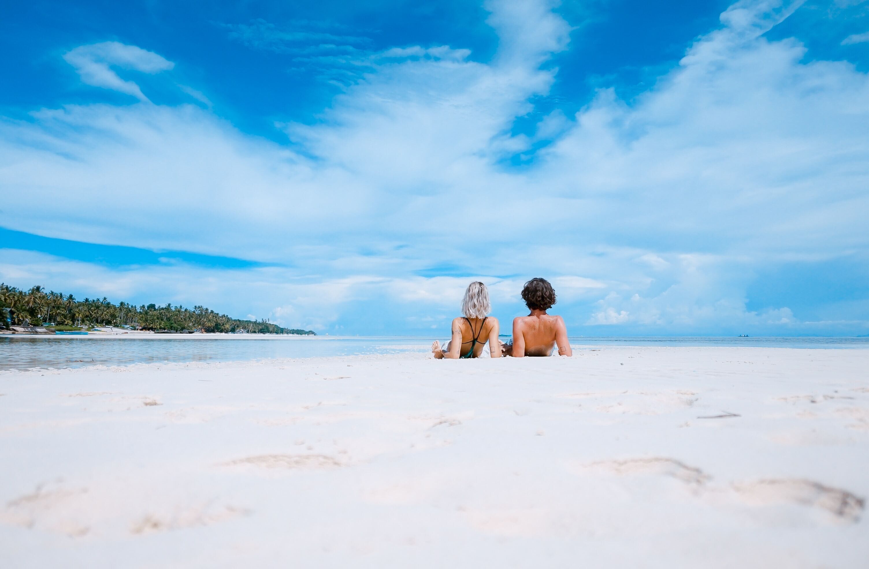 A couple sitting on a beach with a clear sky and ocean in the background.