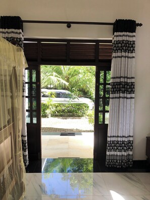 A room with a view of a garden through a door with patterned curtains. - Sri Lankan Villa (Koggala)