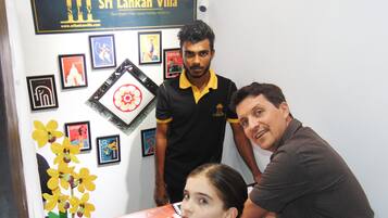 A reception area with framed pictures on the wall, a desk with a flower arrangement, and a sign for Sri Lankan Villa.
