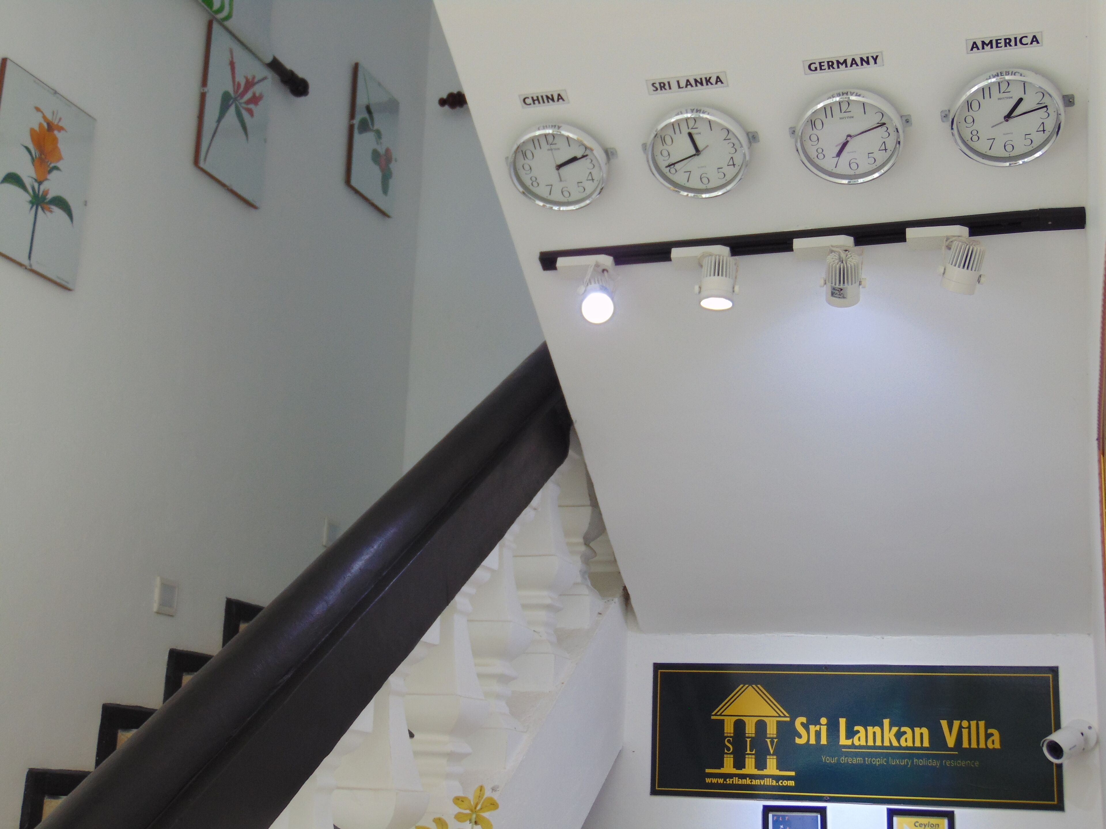 A staircase with a handrail, a wall with clocks labeled with country names, and a sign for Sri Lankan Villa.