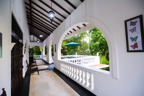 A corridor with white walls, wooden beams, and a balcony with a green umbrella. - Sri Lankan Villa (Koggala)
