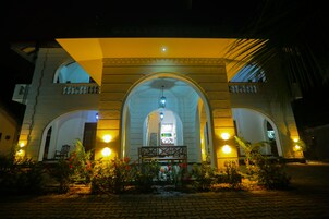 A building with a central archway, a staircase leading to an upper level, and a well-lit entrance area with a bench and plants.