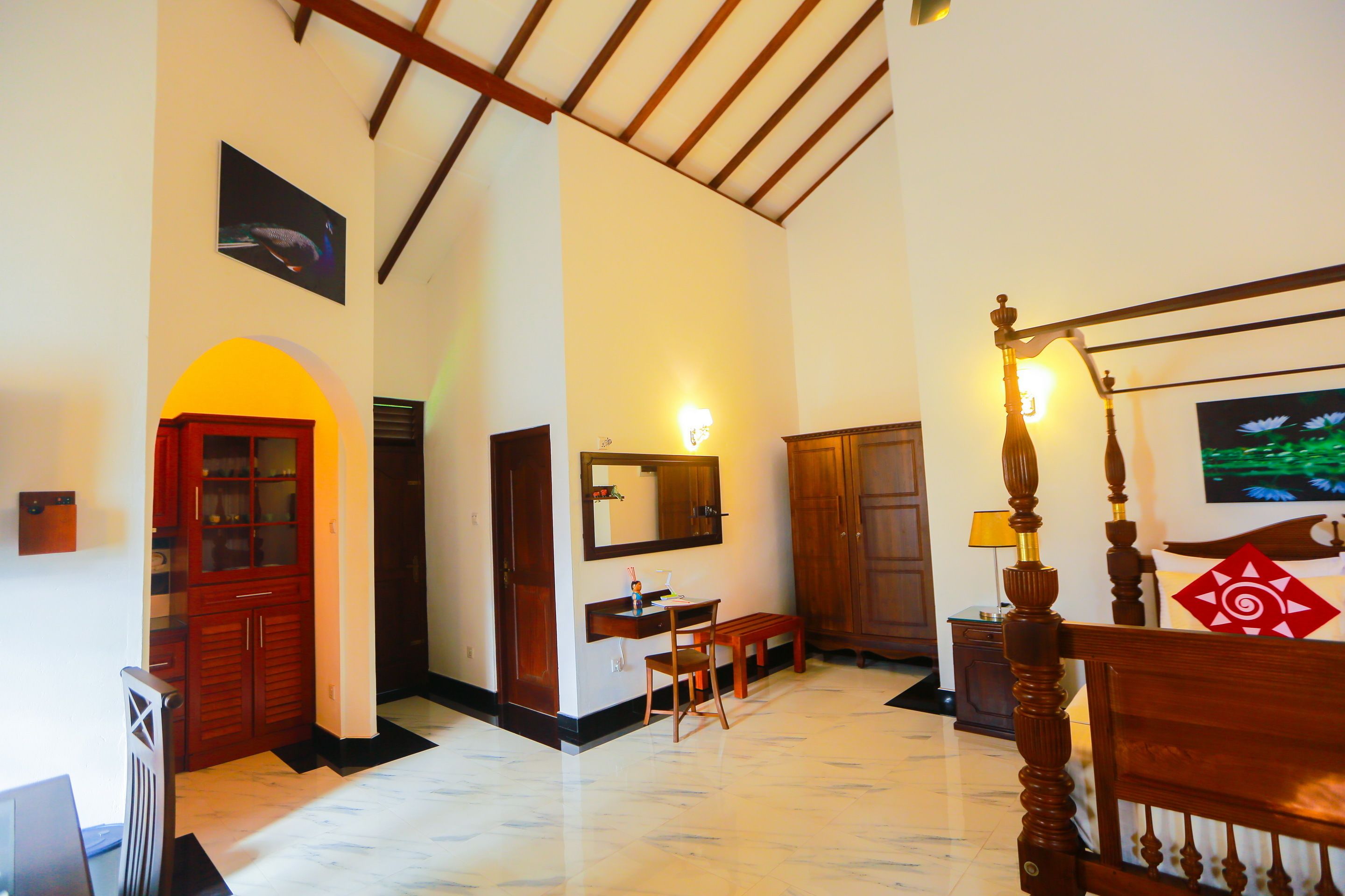 A hotel room with a wooden bed, a desk with a chair, a mirror, a bench, and a TV on the wall.