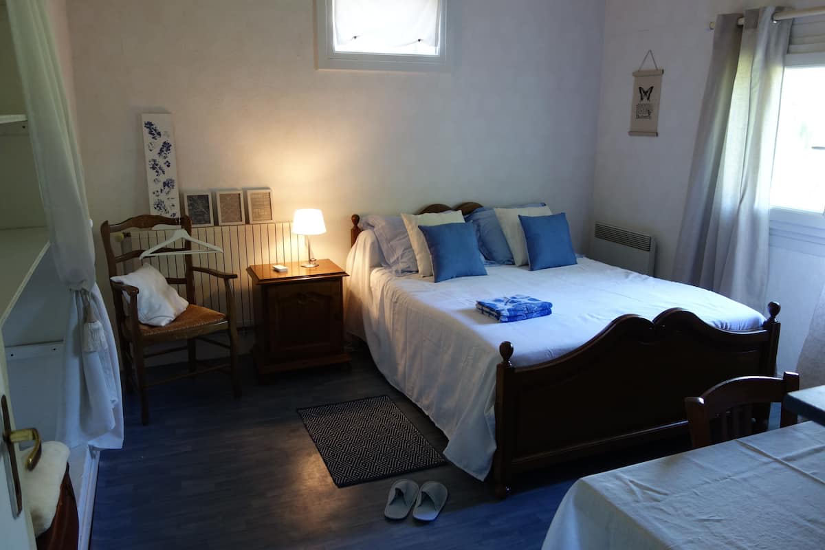 Een slaapkamer met een bed, nachtkastje, lamp en een raam met gordijnen.