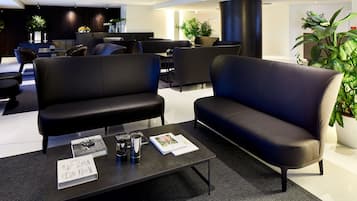 Un'area lounge moderna con divani in pelle nera, un tavolino con riviste e piante in vaso.