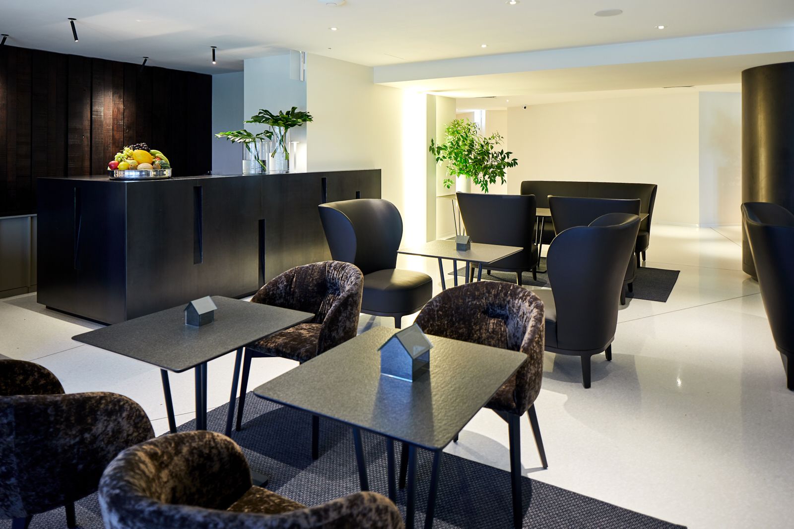A modern lounge area with seating, a reception desk, and a plant.