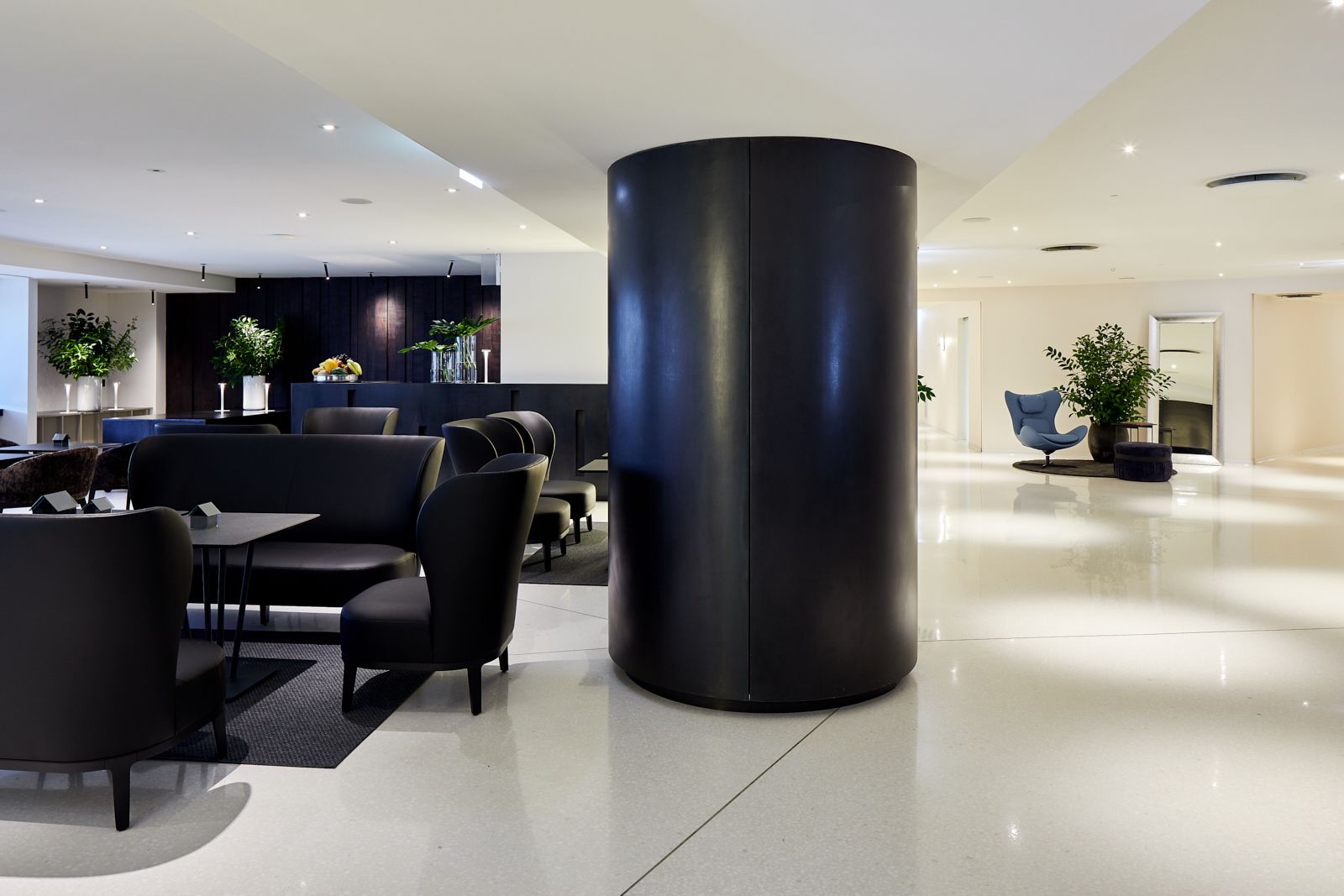 A modern hotel lobby with a large black cylindrical column, seating areas, and a reception desk.