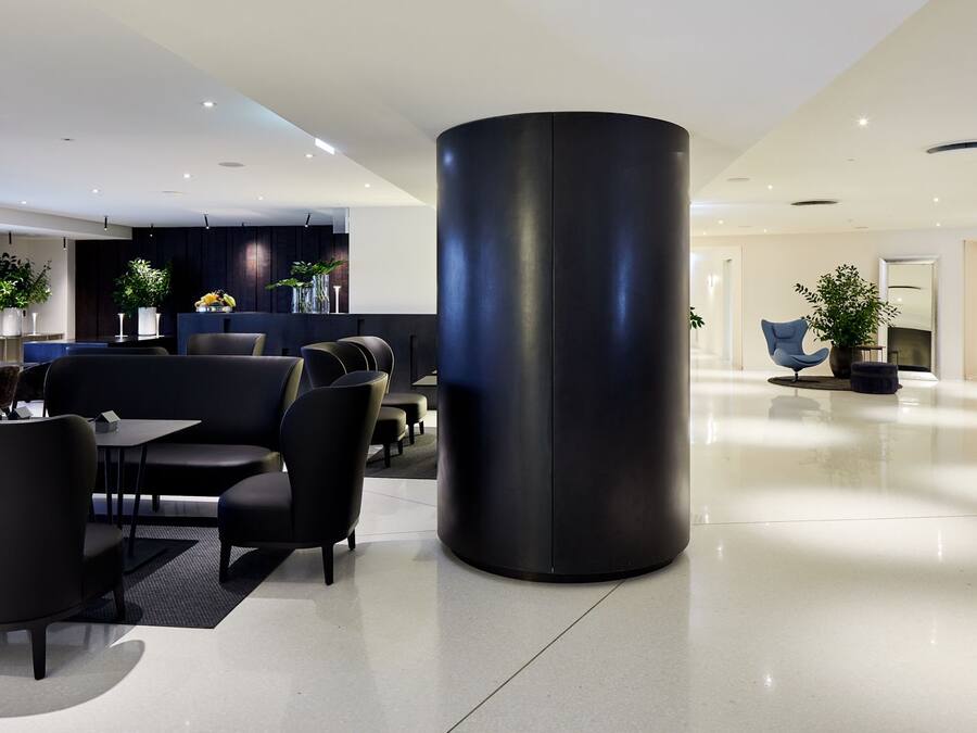 A modern hotel lobby with a large black cylindrical column, seating areas, and a reception desk.