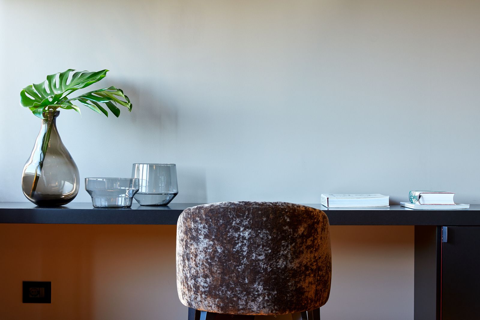 A modern desk with a vase, glass, and books.