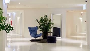 Un hall d’entrée moderne avec un fauteuil bleu, une plante en pot et un pouf noir.