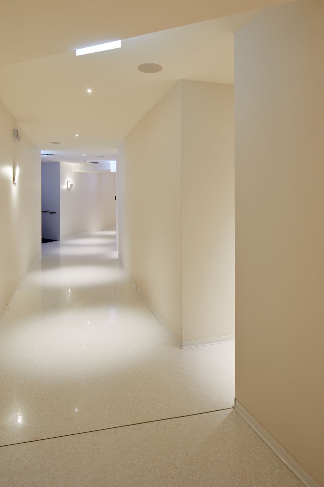 A modern, well-lit hallway with a glossy floor, leading to a room with a door at the end.