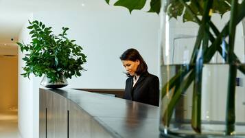 Zona de recepción con recepcionista, un mostrador moderno y una planta grande en maceta.
