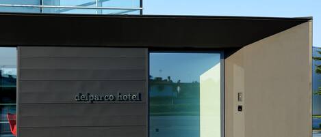 A modern hotel entrance with a dark facade and glass doors, labeled "delparco hotel."