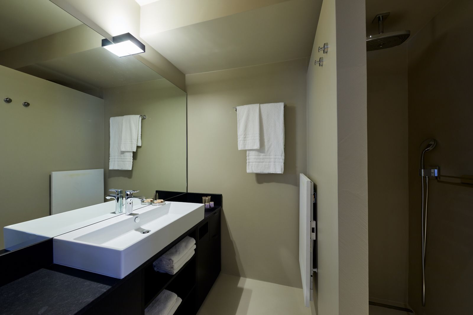 A modern bathroom with a large white sink, a mirror, and a shower area.