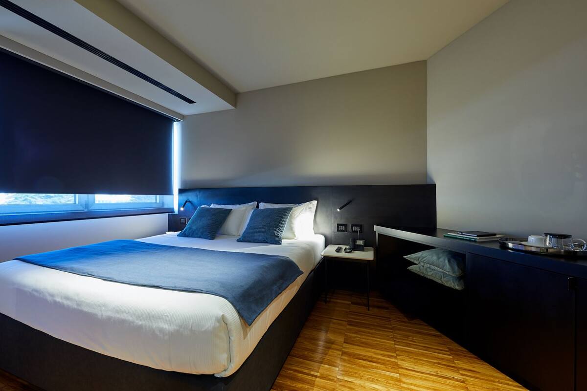 A modern hotel room with a large bed, bedside tables, a desk, and a window.