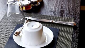 Un tavolo da pranzo apparecchiato con piatti bianchi, posate e una tazza, con un sottopiatti in tessuto.