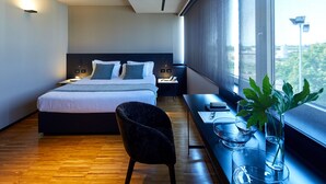 A modern hotel room with a large bed, a desk with a chair, a window with a view, and a plant on the windowsill. - Delparco Hotel (Buttrio)