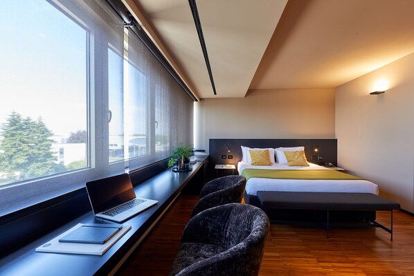 A modern hotel room with a large bed, a desk with a laptop, and a view of the city through large windows. - Delparco Hotel (Buttrio)