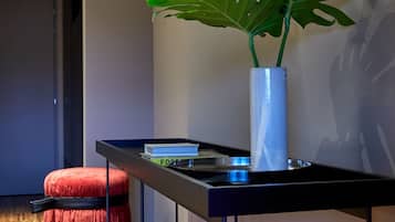 Un espacio habitable moderno con piso de madera, un reposapiés rojo, un jarrón blanco con una planta y una mesa negra con libros.